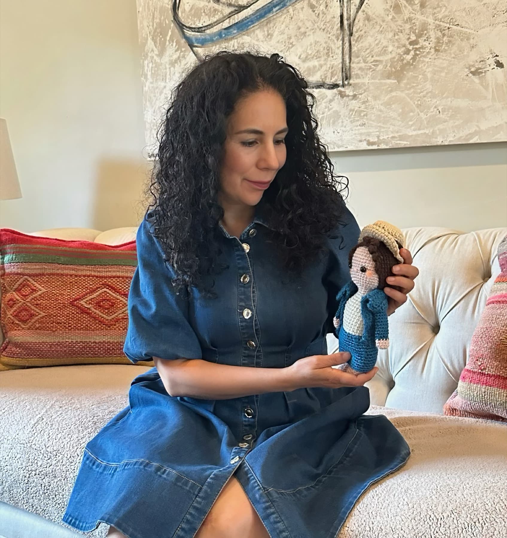 Maria in a denim dress, giving a finished doll one last look